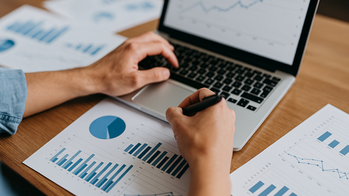 Mãos analisando gráficos de marketing digital em mesa com notebook e relatórios.