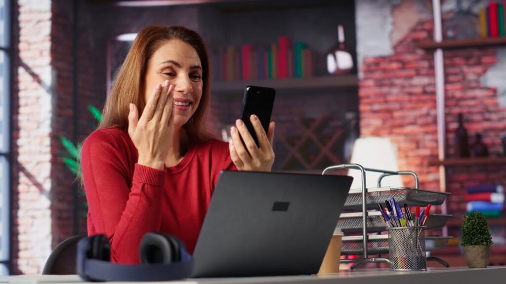 Mulher sorrindo durante chamada de vídeo enquanto trabalha online de casa.